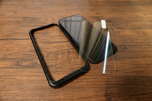 NIMASOガラスフィルムと貼り付け用ガイド枠をiPhone 18 Proの横に並べたところ