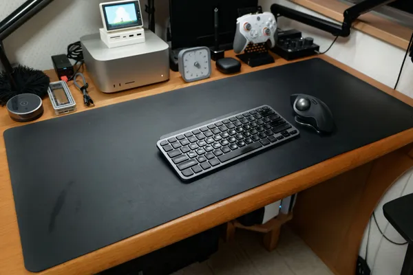 木製デスクに黒い大型デスクマットを敷き、キーボードとトラックボールマウスを置いた様子