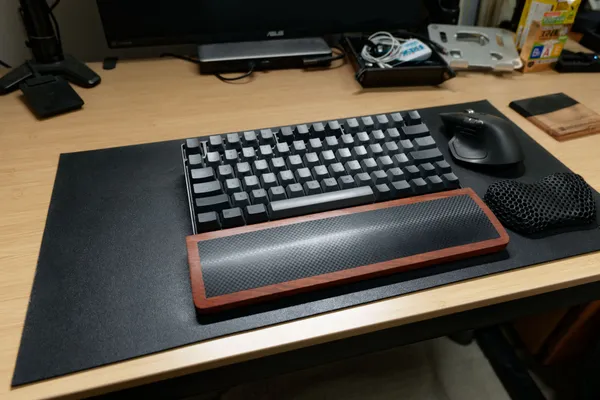 黒いデスクマットの上にキーボードと木製パームレスト、マウスを置いた竹天板のデスク