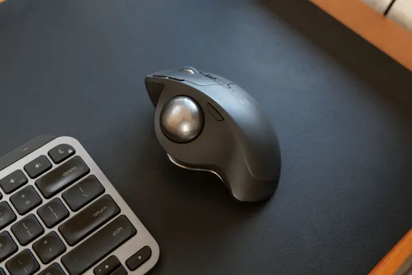 黒いデスクマットの上で、キーボードの横に置いたトラックボールマウス MX ERGO S