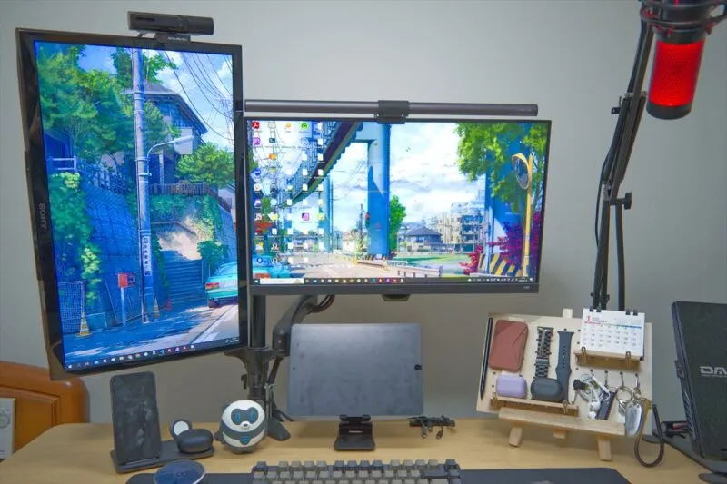 デュアルモニターに異なる風景画像を表示したデスク全体。マイクや周辺機器も設置