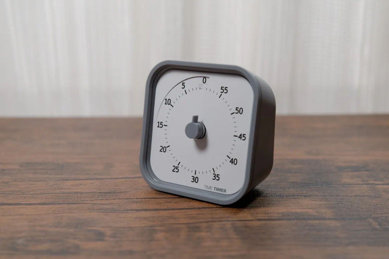 Time Timerを白いカーテンを背景に木目デスクへ斜めに置いた本体全体（残り時間0分）